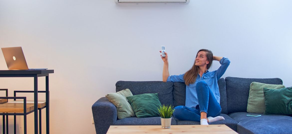 Young happy woman sitting on couch under air conditioner and adj