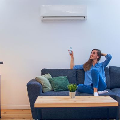Young happy woman sitting on couch under air conditioner and adj